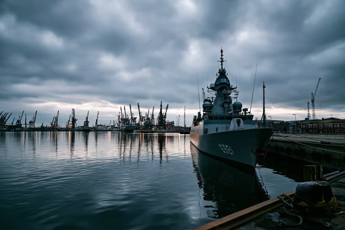 Pilka karinio jūrų laivyno dokų teritorija apsiniaukusiu dangumi, rodanti investicijas į gynybą.